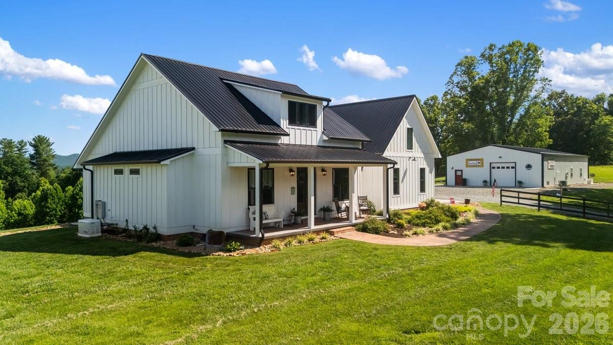 White farmhouse with dark metal roofs and a covered porch beside a detached outbuilding.