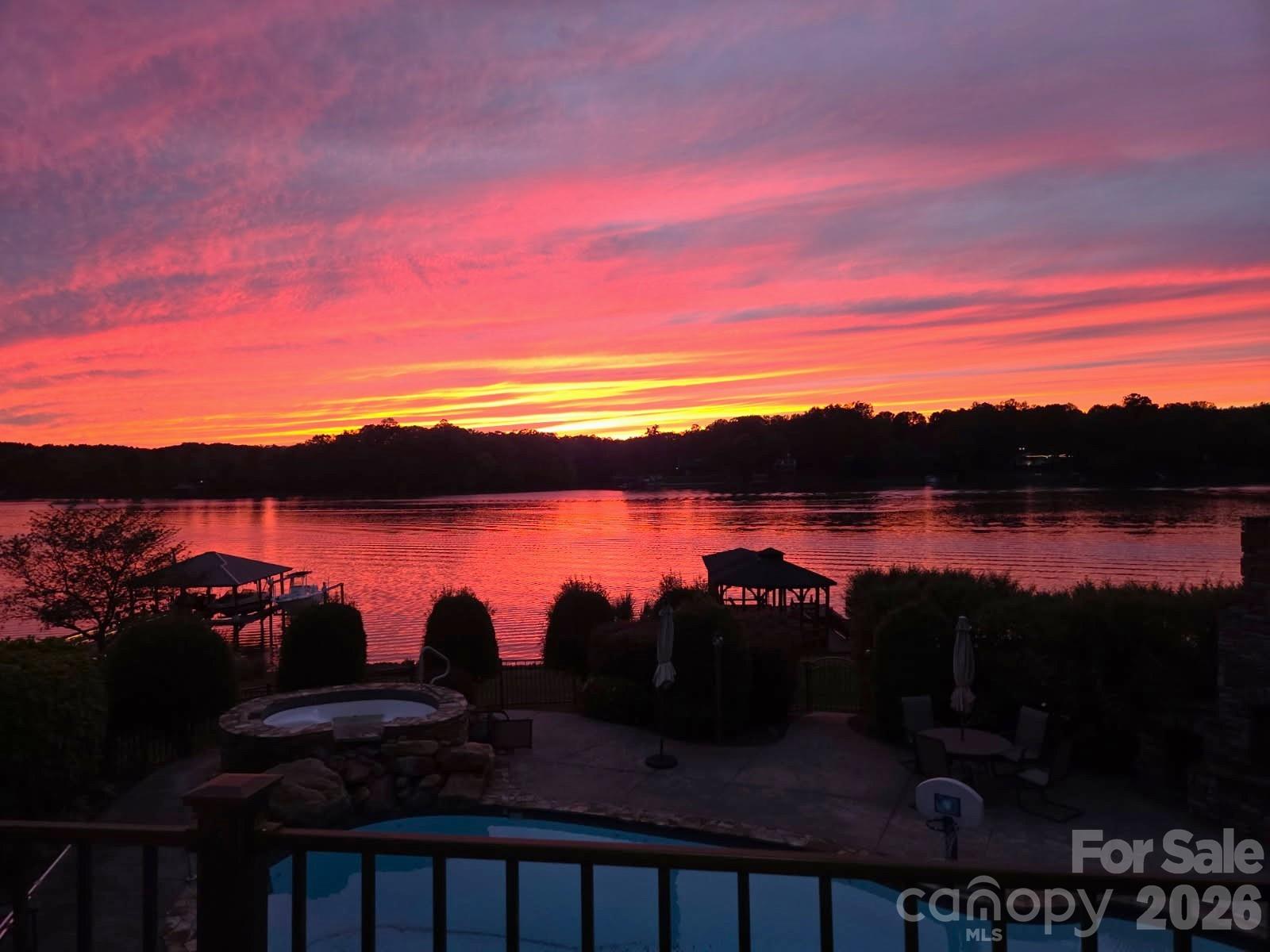 Lakefront backyard at sunset with a pool, stone spa, patio, and docks.