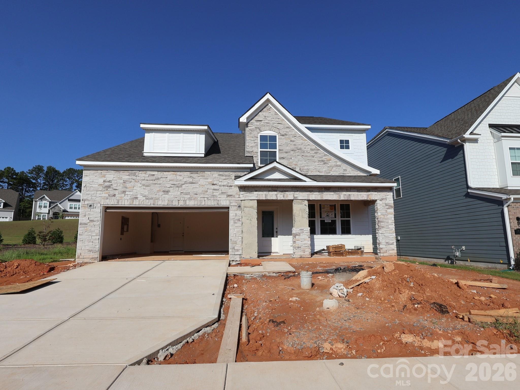 Stone-and-white two-story house under construction, with an open garage and unfinished landscaping.