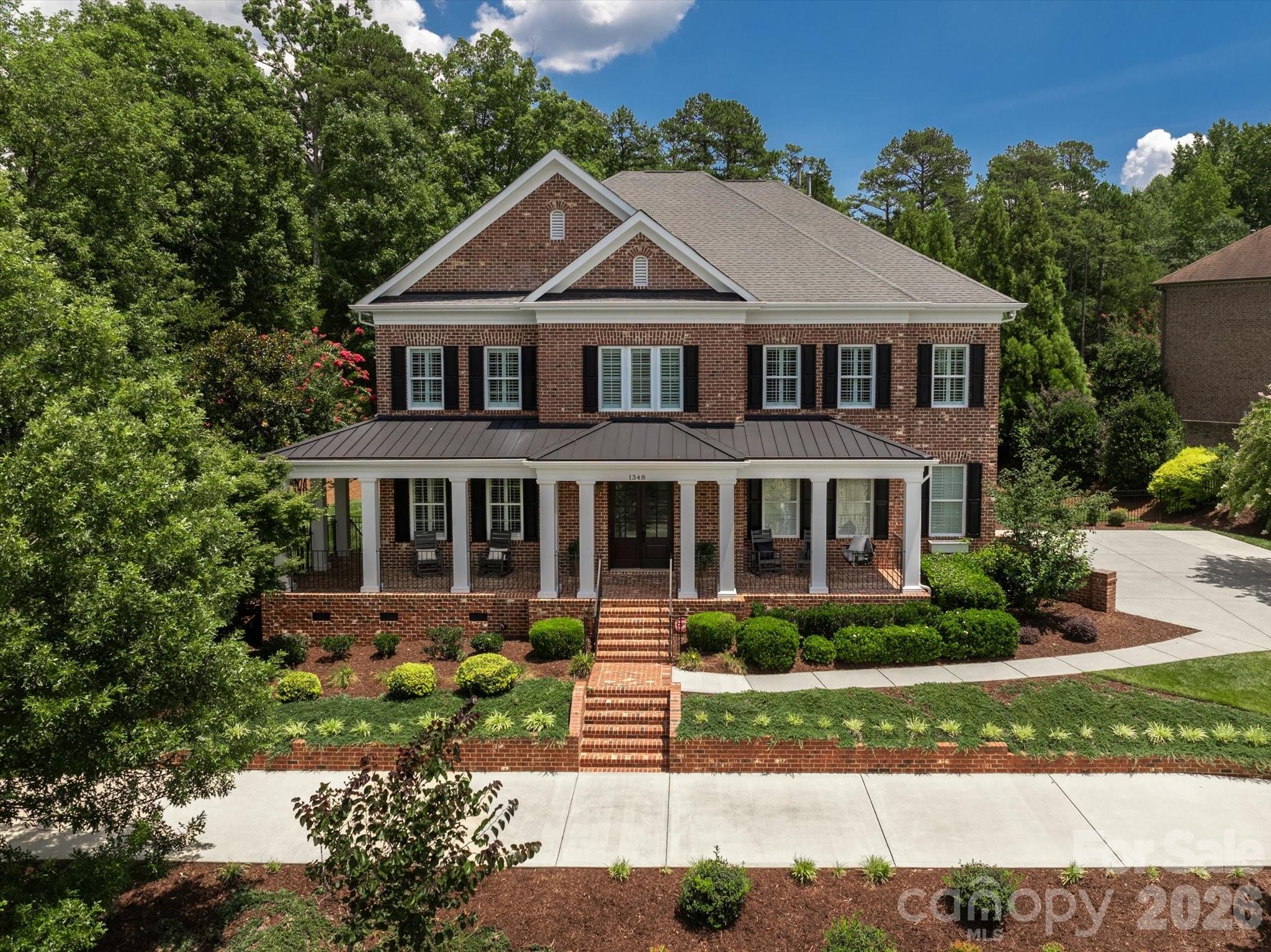 Two-story brick house with a broad covered porch, black shutters, and landscaped front beds.