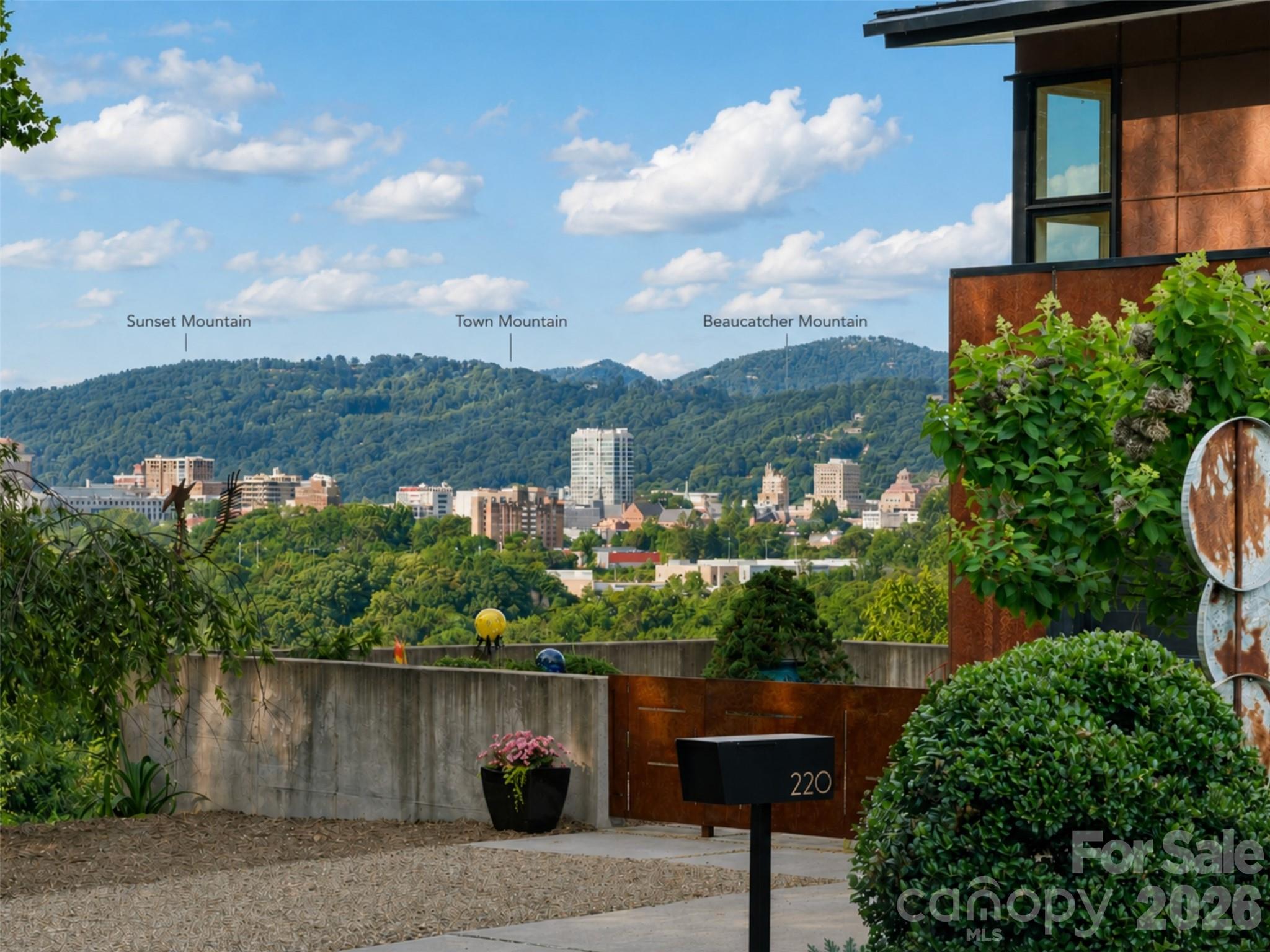 Modern home entrance overlooking Asheville’s skyline and wooded mountains, with Sunset, Town, and Beaucatcher Mountains labeled.