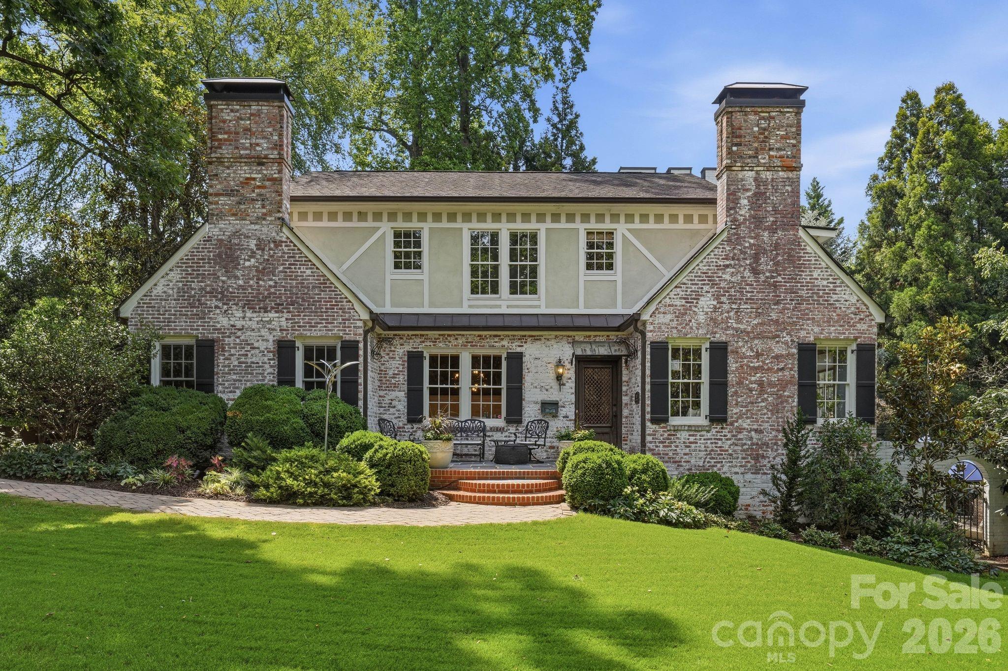 Two-story brick-and-stucco home with twin chimneys, a landscaped garden, and a broad front lawn.