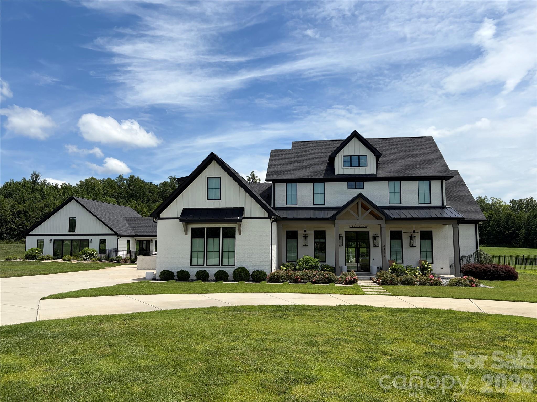White two-story home with black trim, multiple gables, landscaped beds, and a broad front lawn.