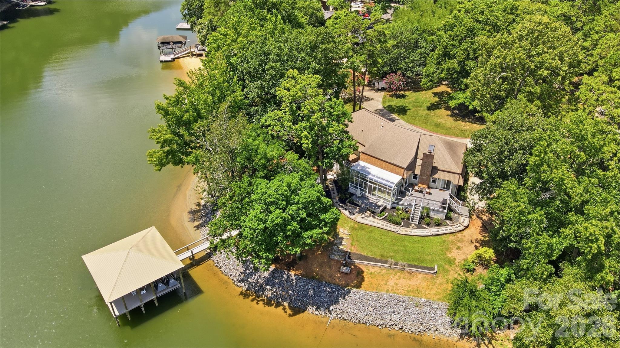 Aerial view of a wooded lakefront home with a screened porch, deck, and covered dock.