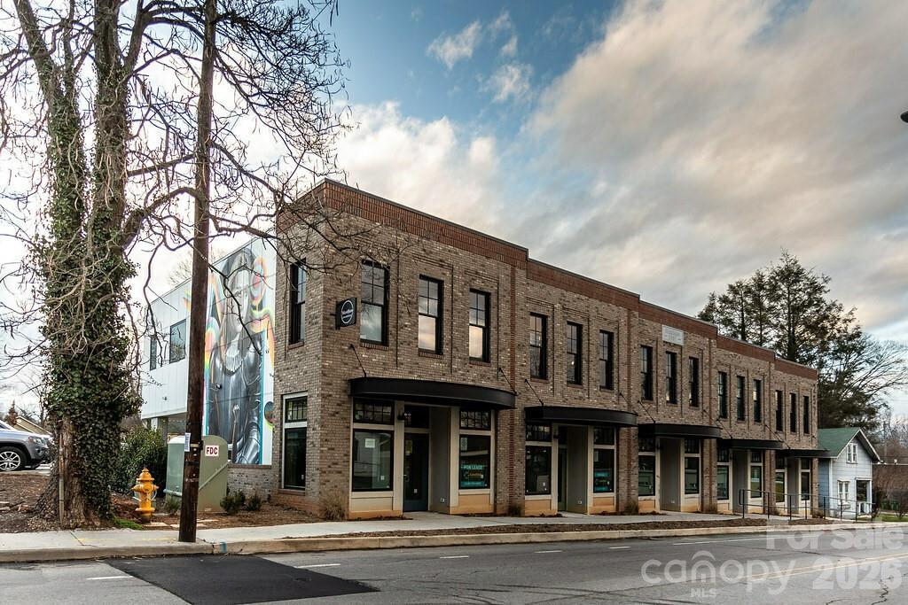 Two-story brick commercial building with multiple storefronts and a colorful mural on its side wall.