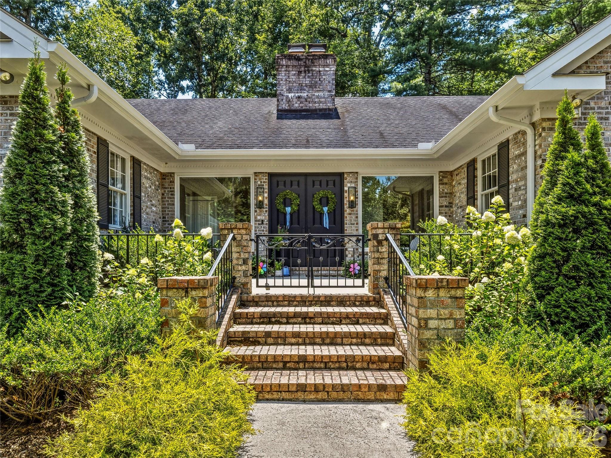 Brick home entrance with wreath-adorned double doors, broad brick steps, and lush landscaping.