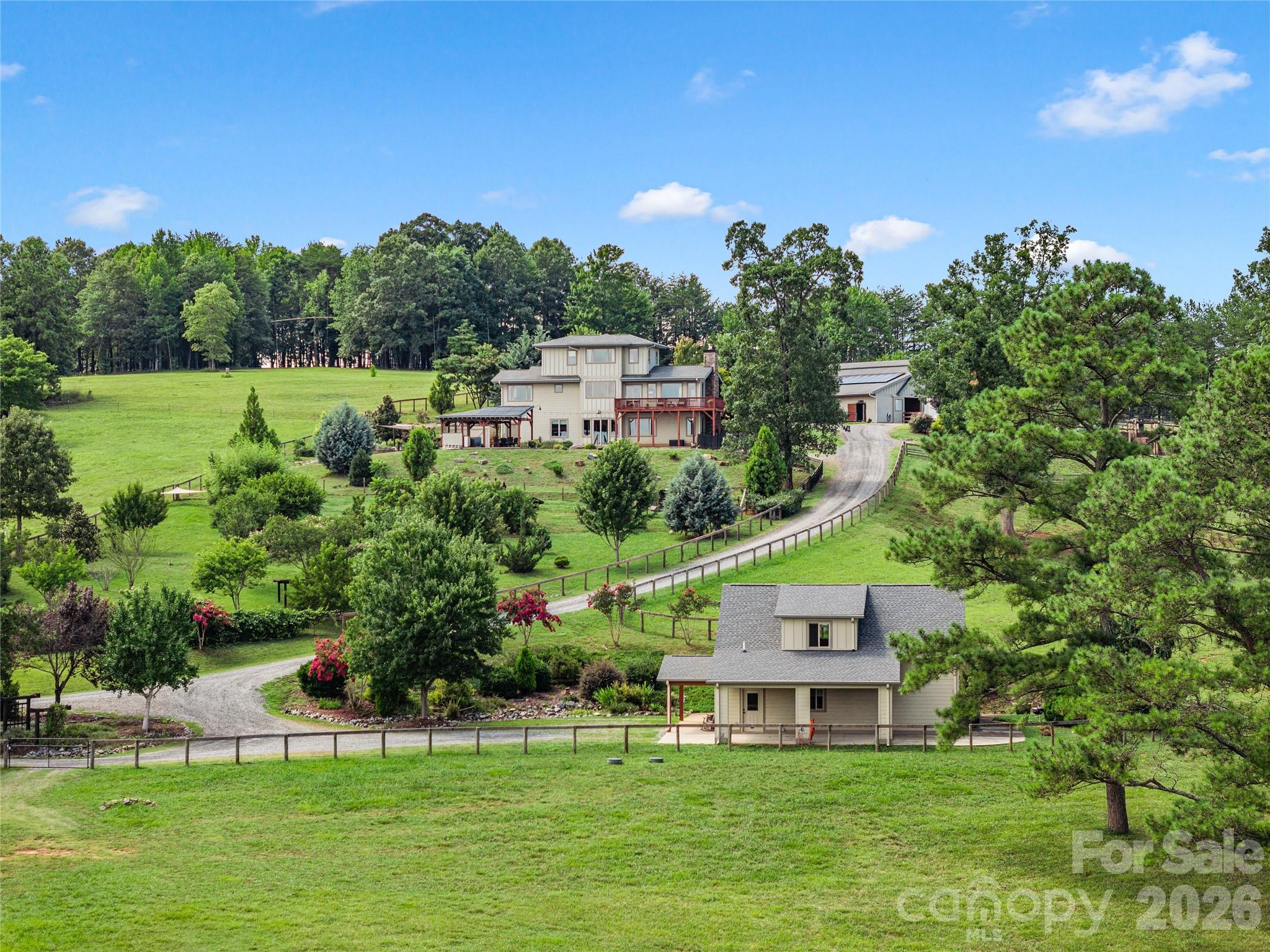 Rural property with several houses, a curving gravel drive, fenced lawns, and mature trees.