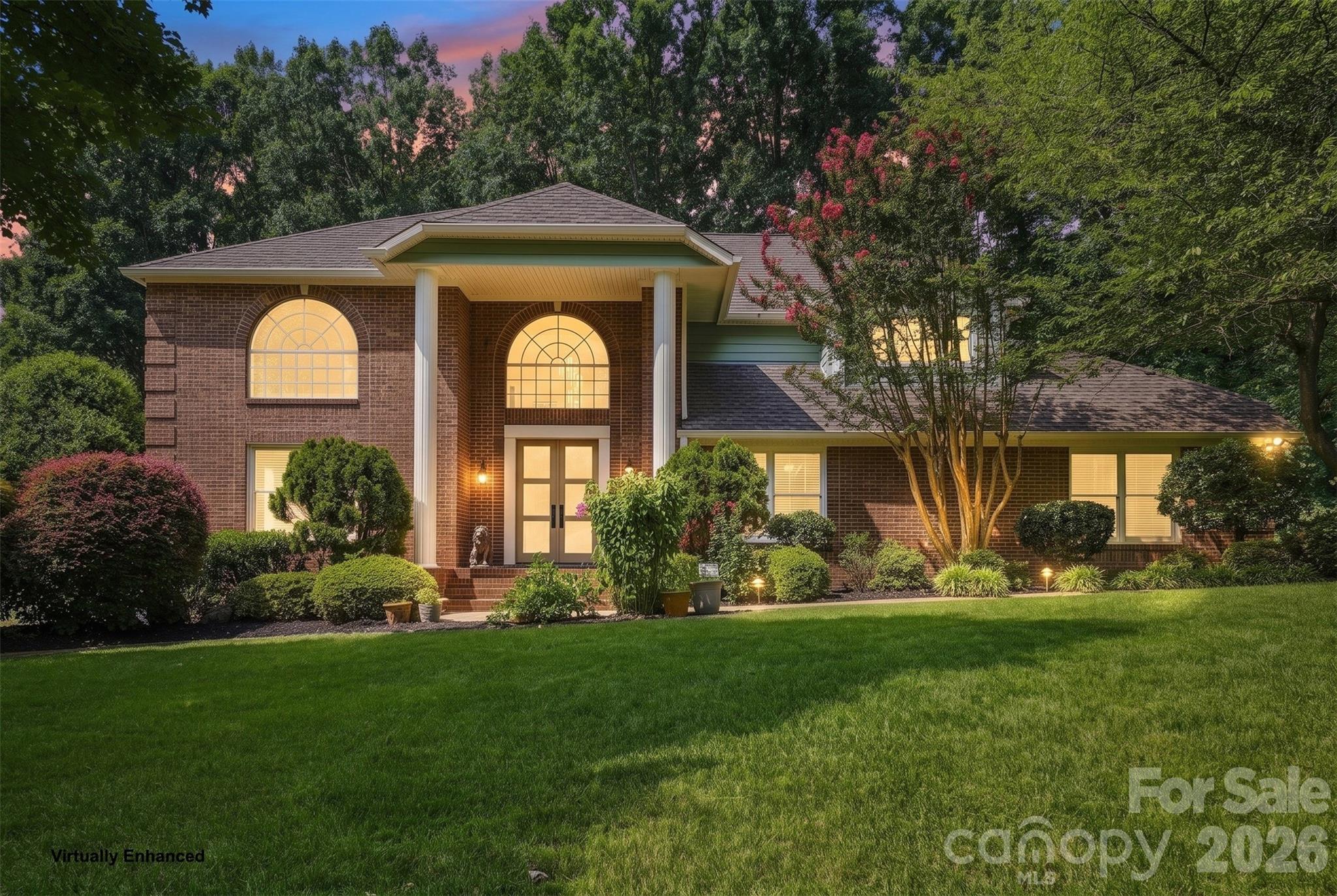 Brick house with white columns, arched windows, and landscaped lawn at dusk.