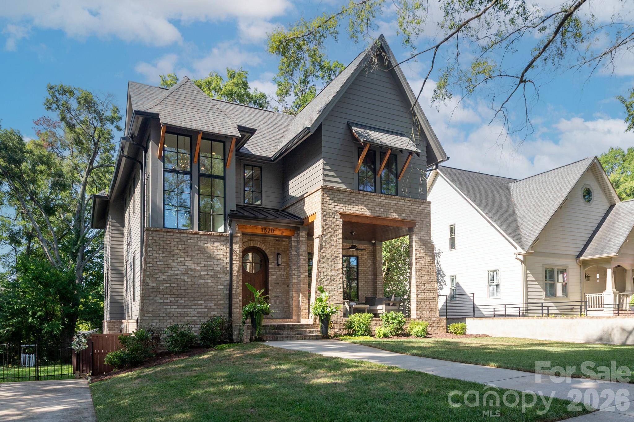 Two-story gray-and-brick home with tall windows, a covered porch, and a steep gabled roof.