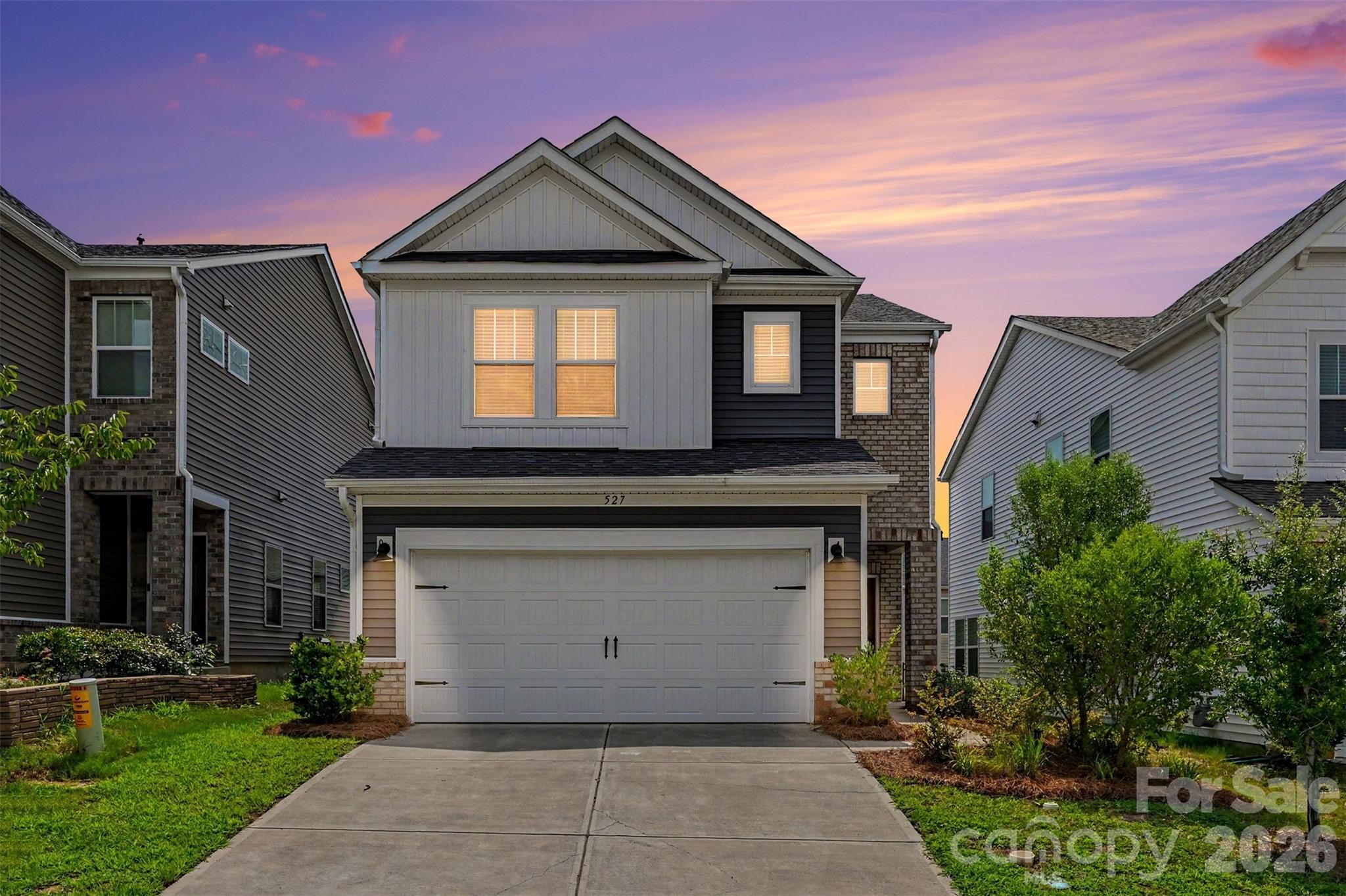 Two-story house with a double garage and glowing windows beneath a pink dusk sky.