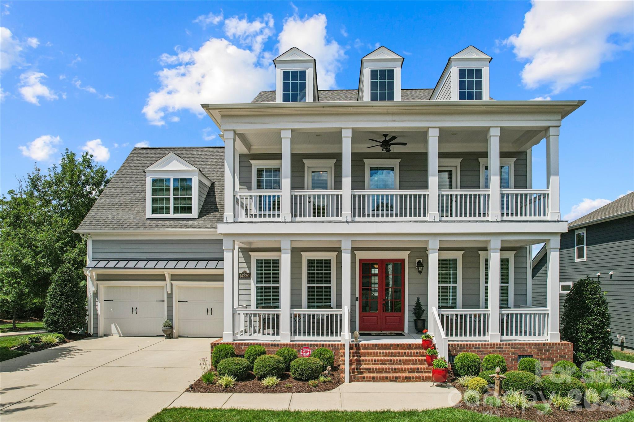 Gray two-story house with white trim, a broad covered porch, red doors, and a two-car garage.