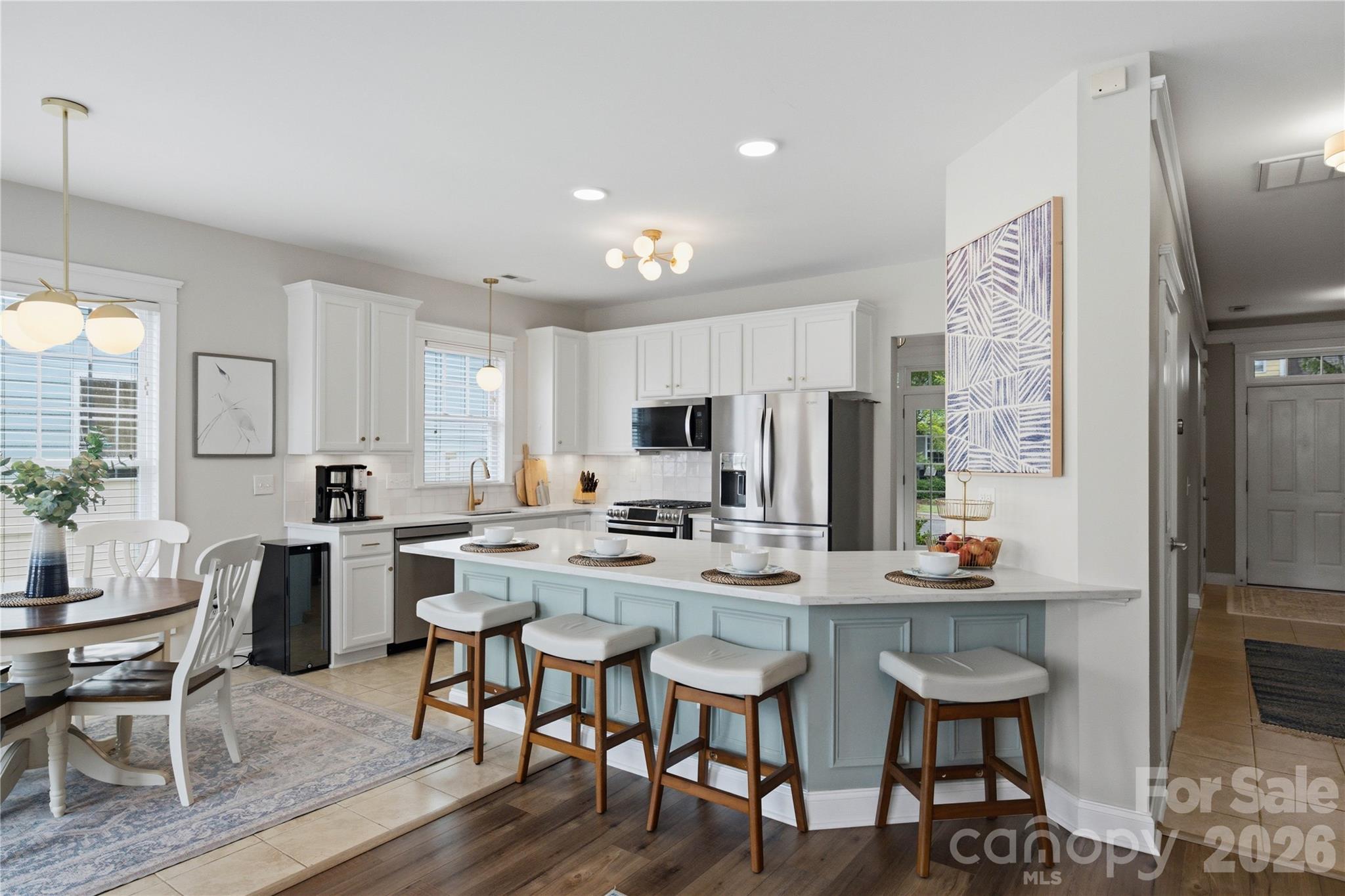 Open-plan kitchen with white cabinets, stainless appliances, and a pale blue island with four bar stools.