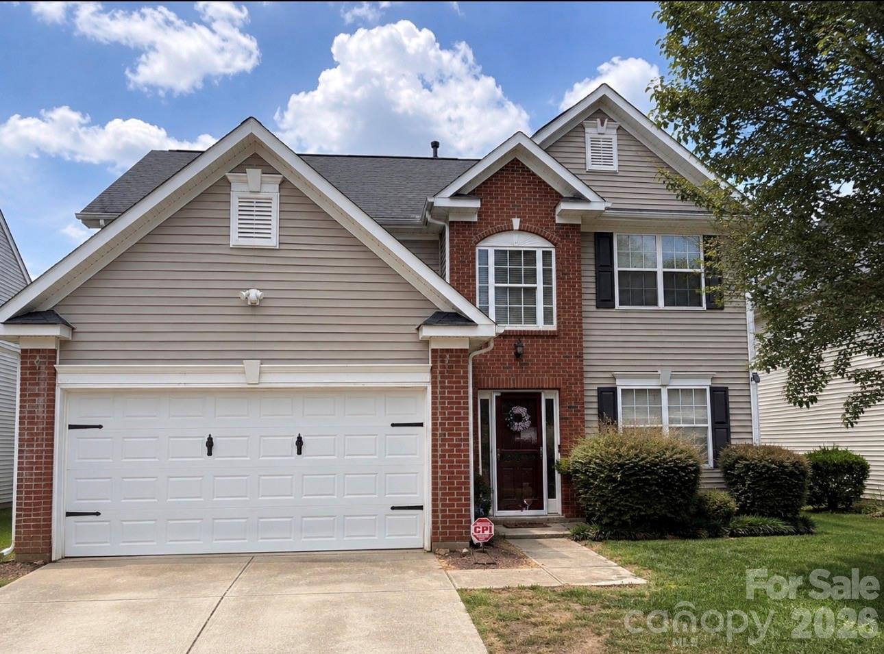 Two-story house with beige siding, red brick accents, and a wide double garage.