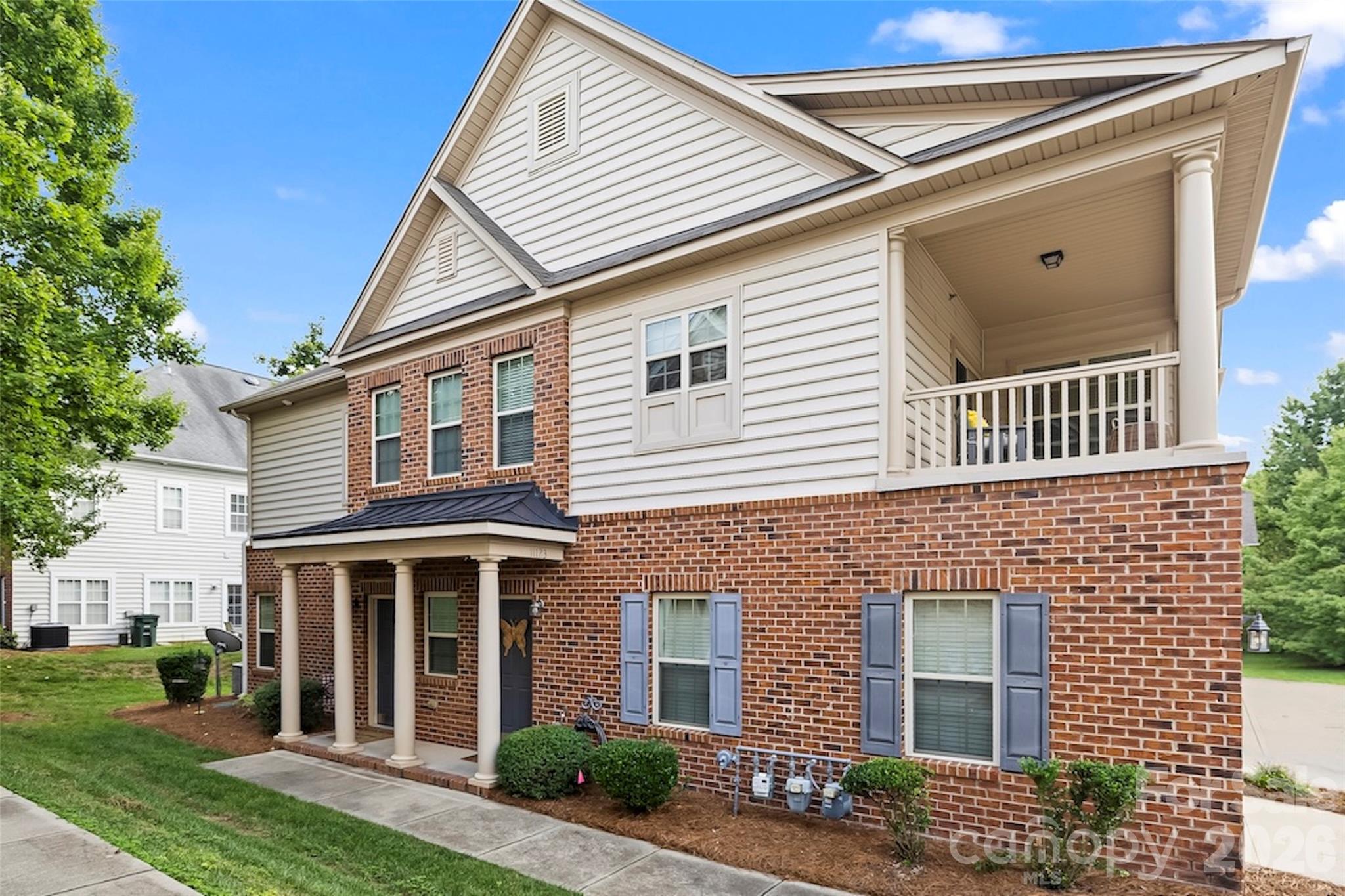 Two-story brick and white-sided house with a covered front porch and upper-level balcony.