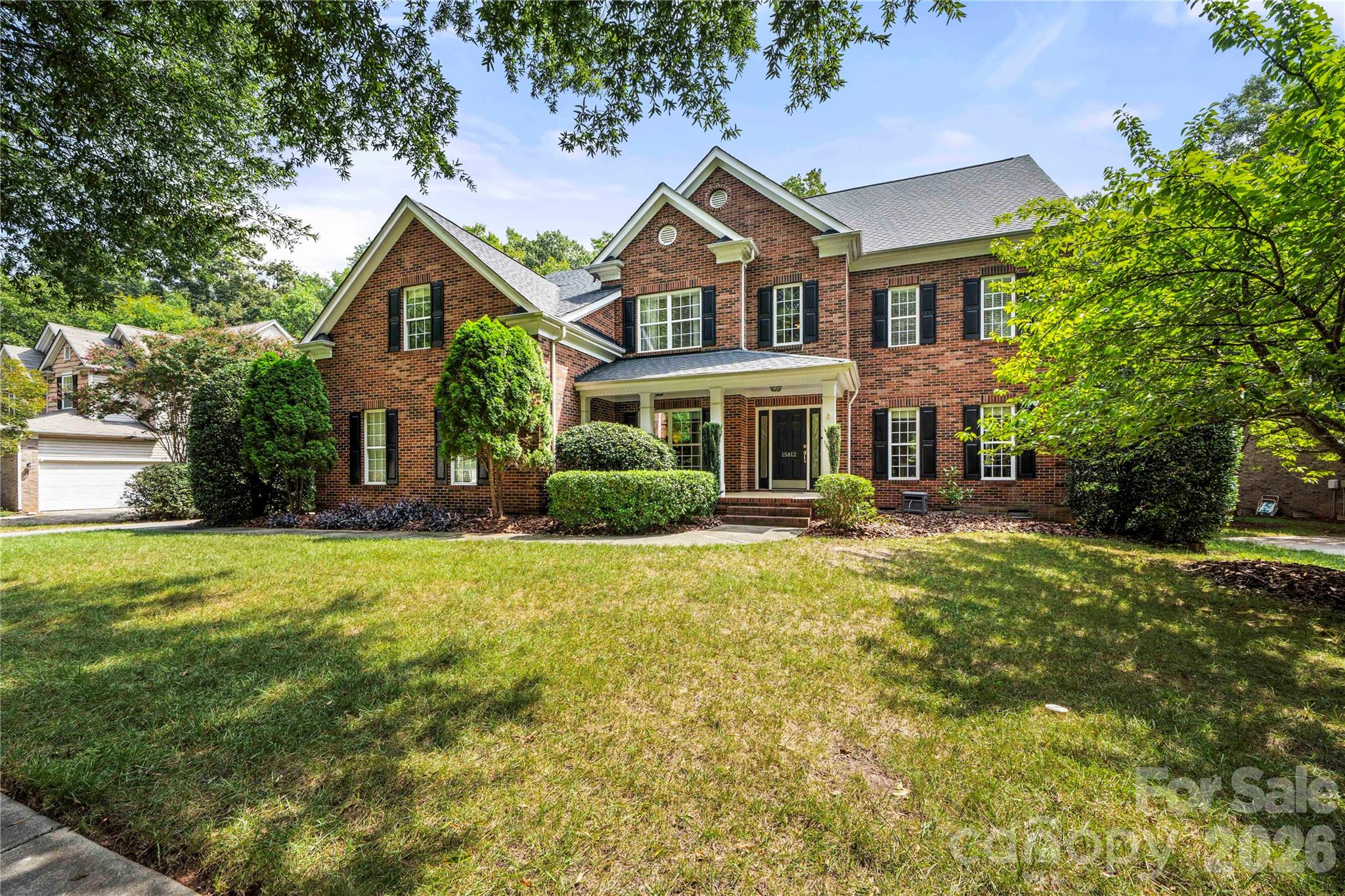 Two-story brick house with black shutters, a covered porch, and a broad front lawn.