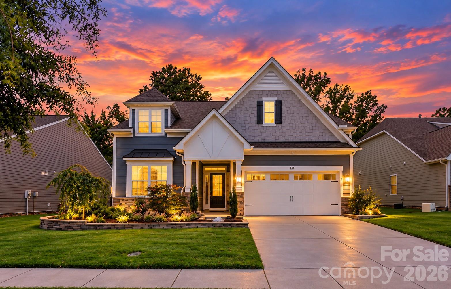 Two-story gray home with a two-car garage and landscaped yard under a vivid sunset.
