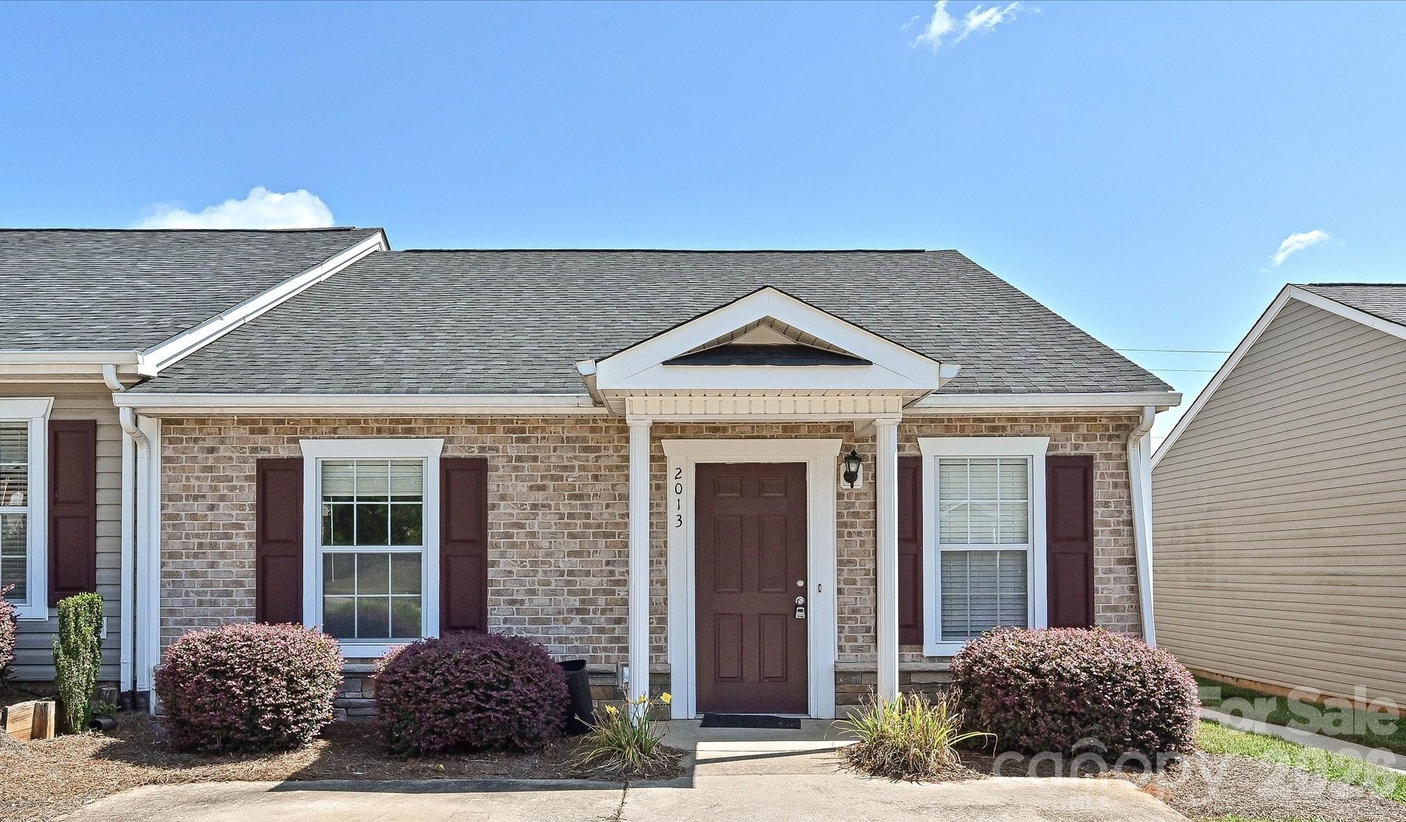 Single-story brick home with a covered entry, burgundy shutters and landscaped front walkway.