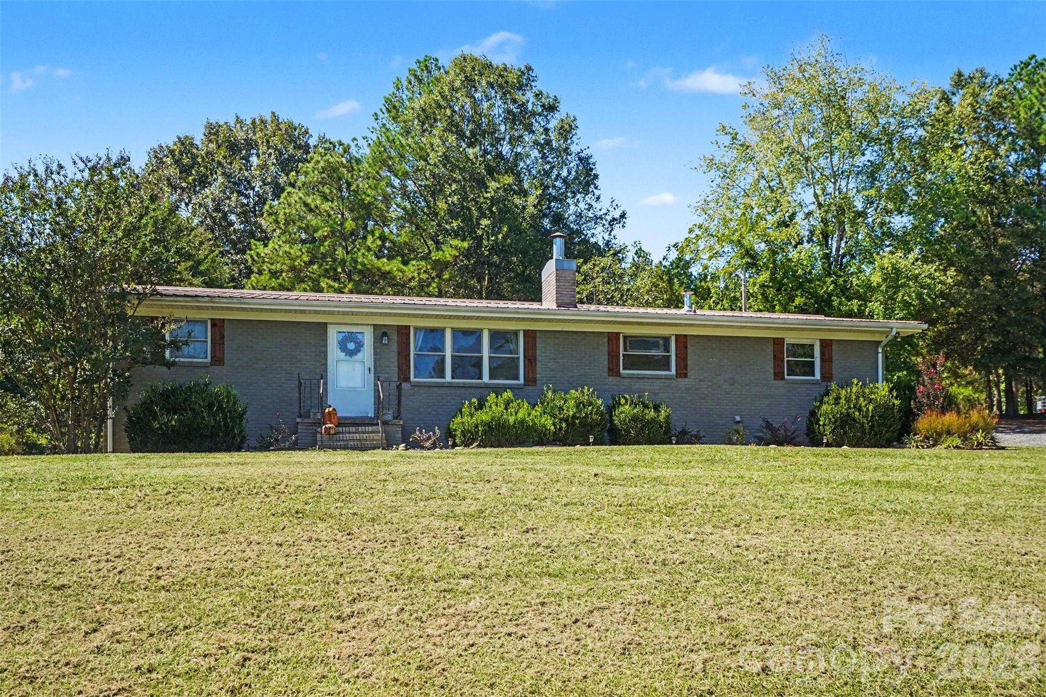 Single-story brick ranch with a white front door, shuttered windows, and a broad sloping lawn.