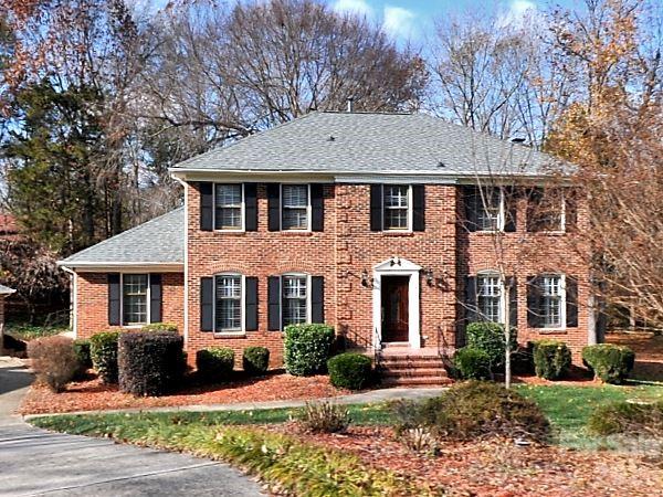 Two-story brick home with black shutters, front steps, trimmed shrubs, and a driveway.