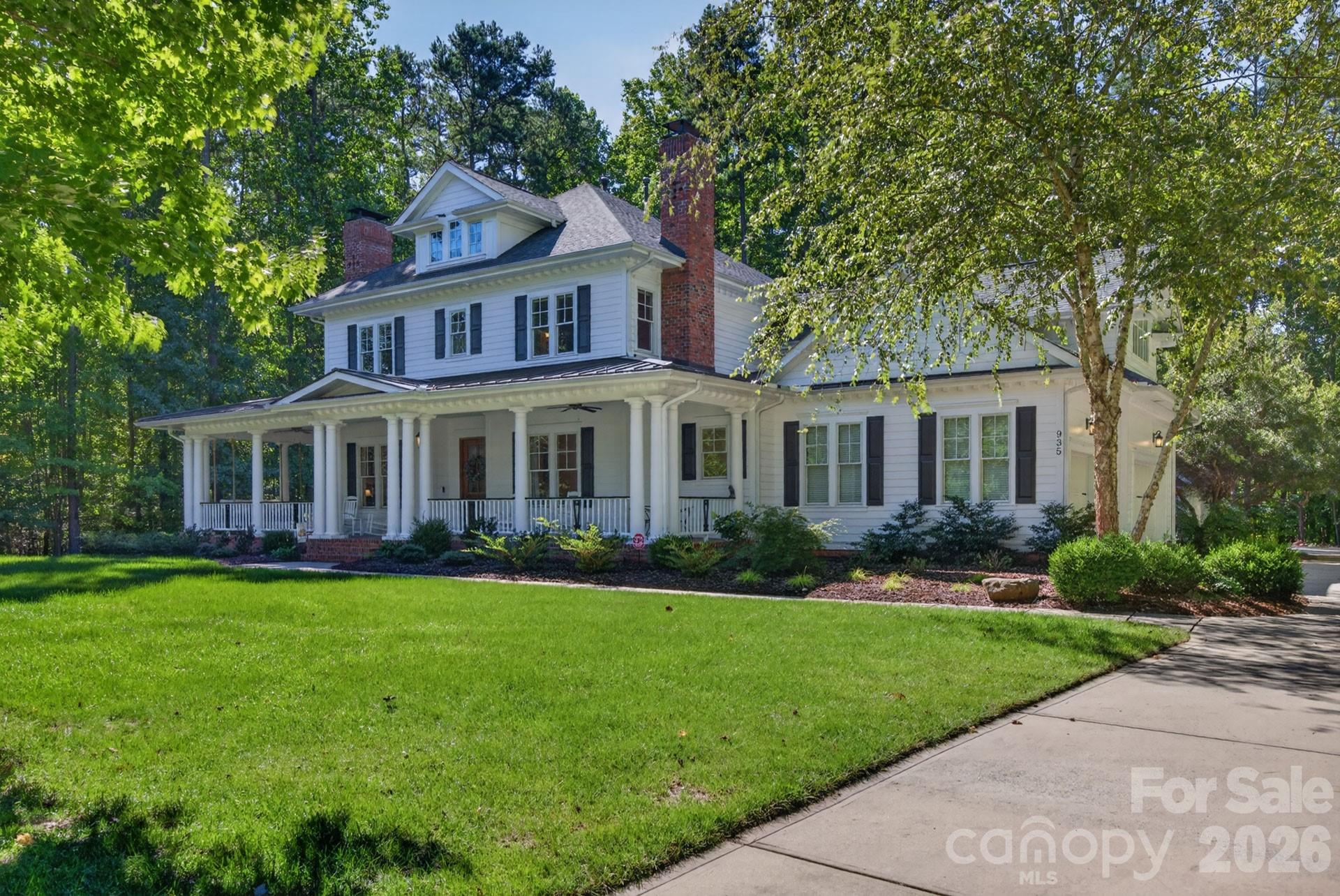White two-story house with a columned porch and brick chimneys beneath mature trees.