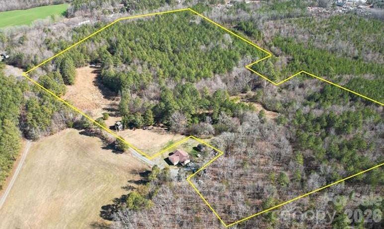 Aerial view of a wooded property with open fields, a small house, and yellow boundary lines.