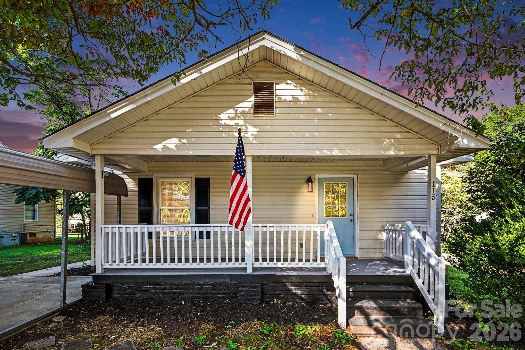 Beige gabled house with a covered white porch, blue door, and American flag.