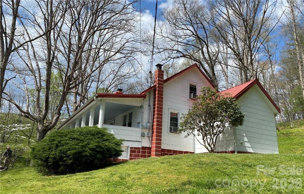 White hillside house with red metal roofs, brick chimney, and a covered porch among trees.