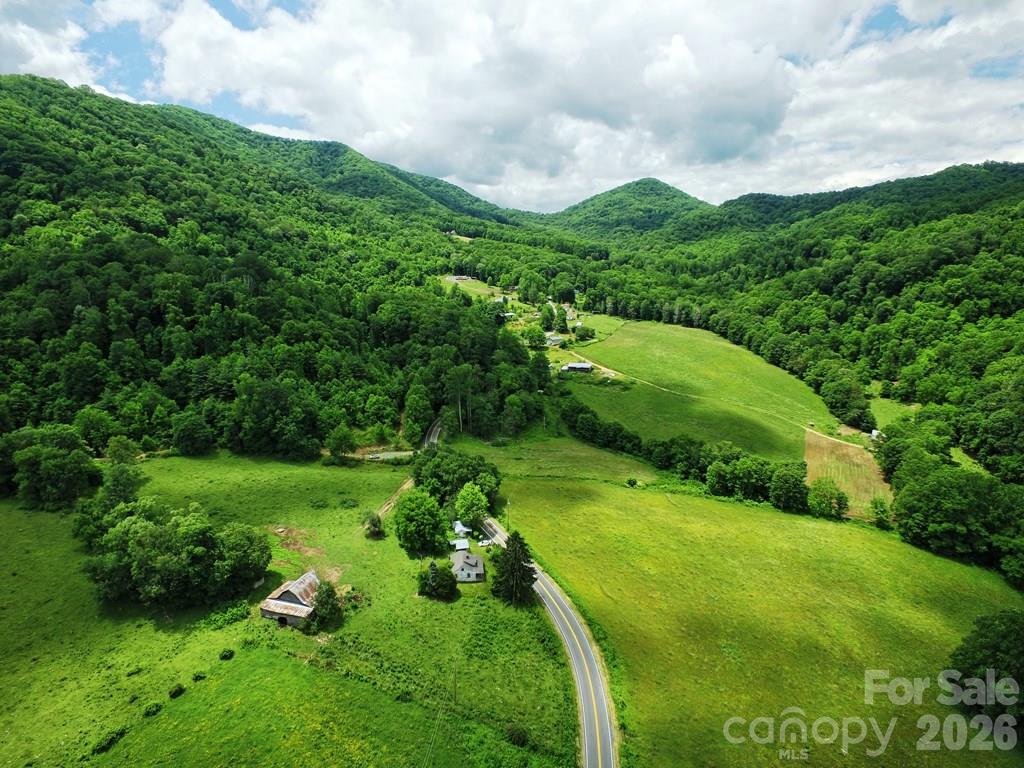 Aerial view of a rural valley with forested ridges, open fields, scattered homes and a winding road.