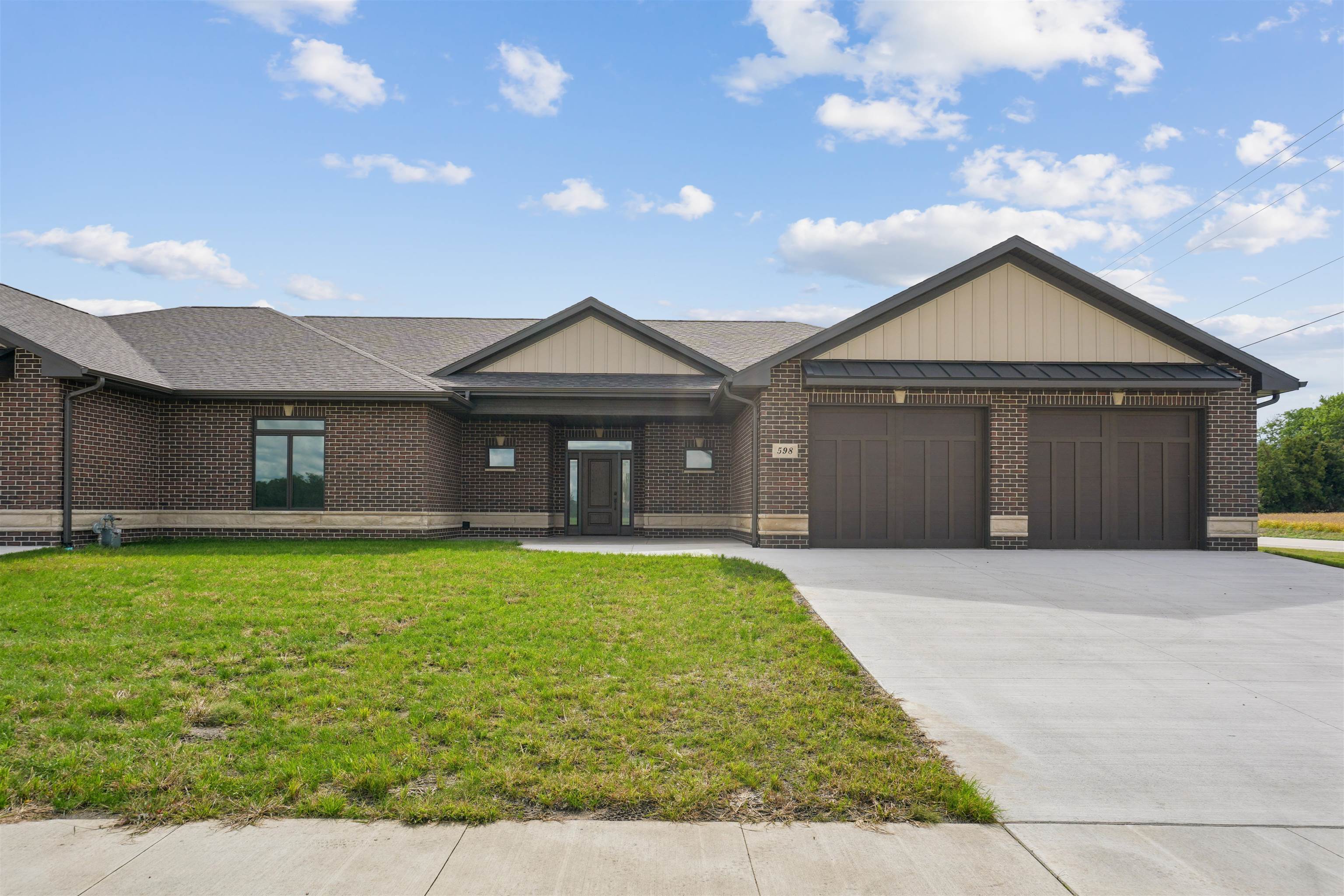 Single-story brick house with light gables, a two-car garage, and a broad concrete driveway.