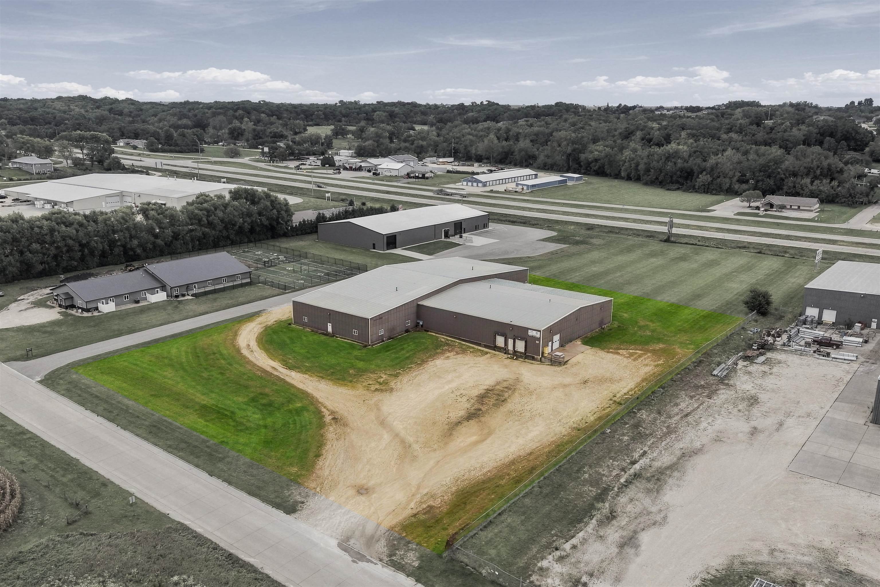 Aerial view of a commercial complex with large metal buildings, service yards, and wooded hills beyond.
