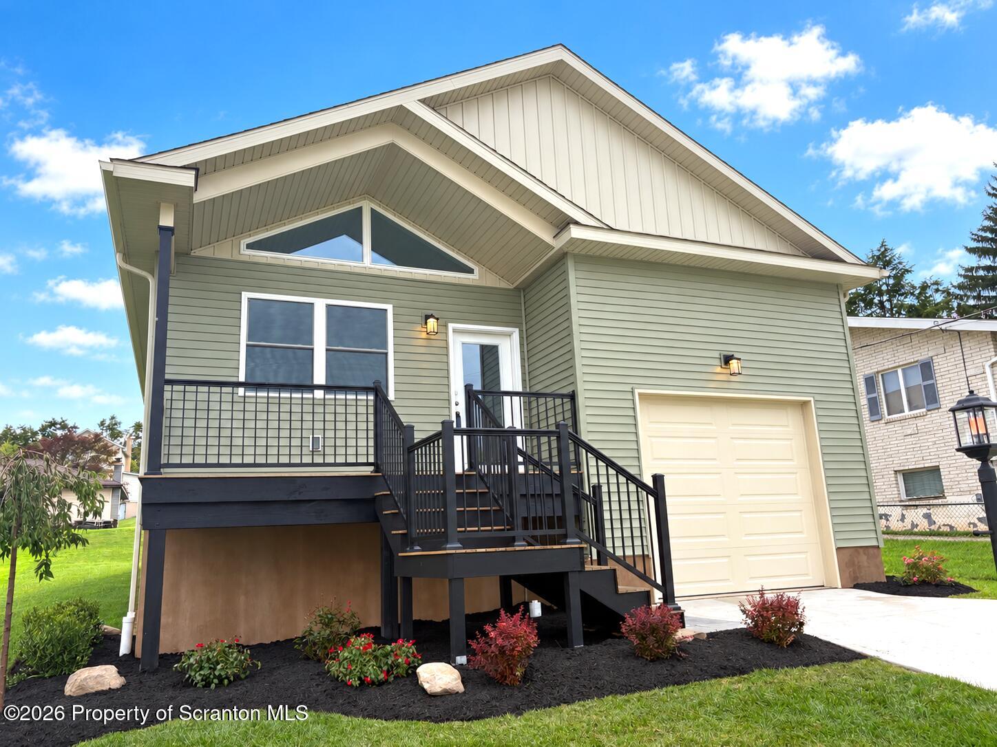Sage-green home with a black-railed front deck, exterior stairs, and attached garage.