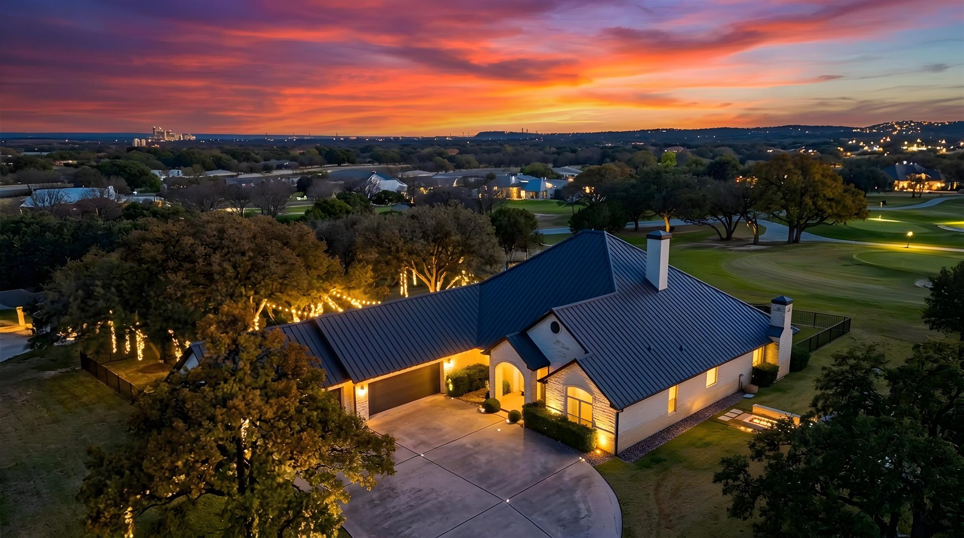 Aerial view of a warmly lit home beside a golf course at sunset.
