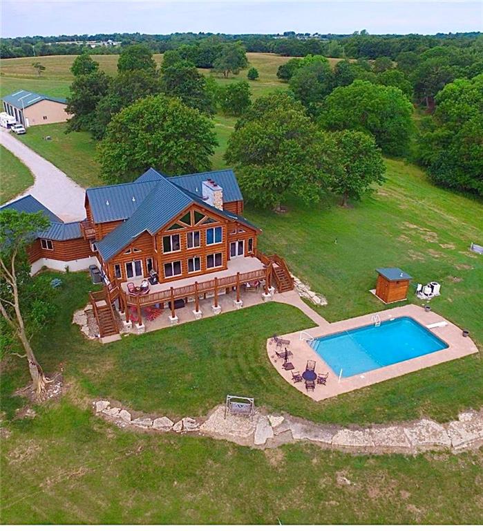 Rural timber-style home with blue roofs, a wraparound deck, and an outdoor swimming pool.