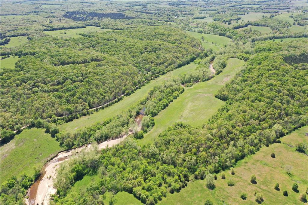 Aerial view of wooded countryside and open fields divided by a winding creek.