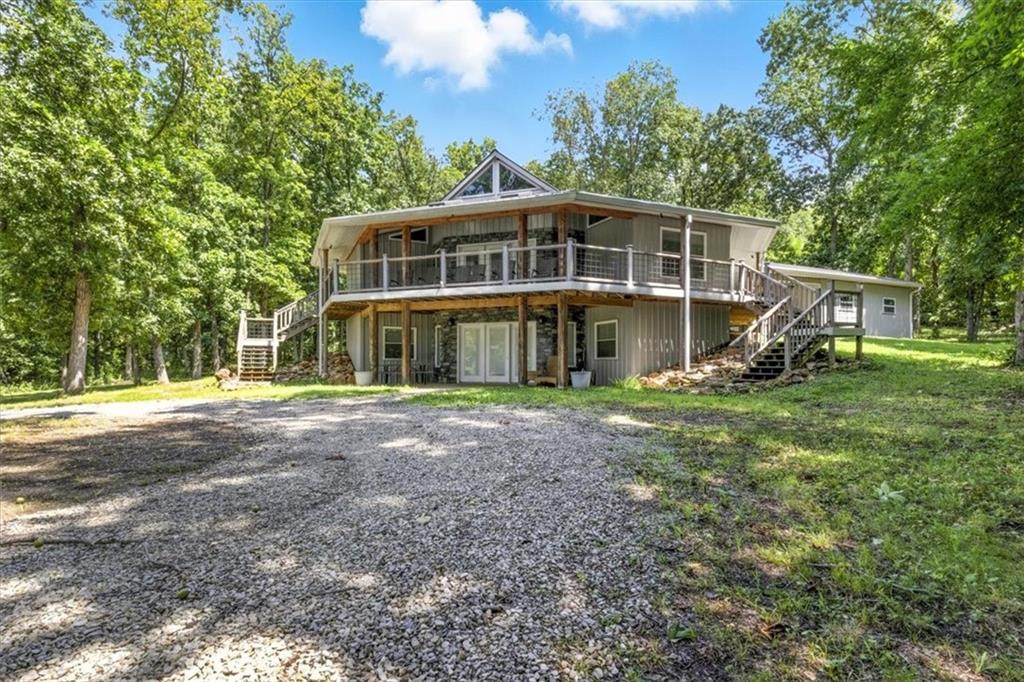 Two-story home with a wraparound deck and exterior stairs, surrounded by trees.