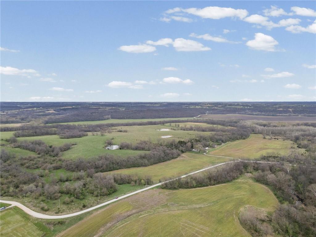 Aerial view of rolling farmland, wooded areas, small ponds, and a winding country road.