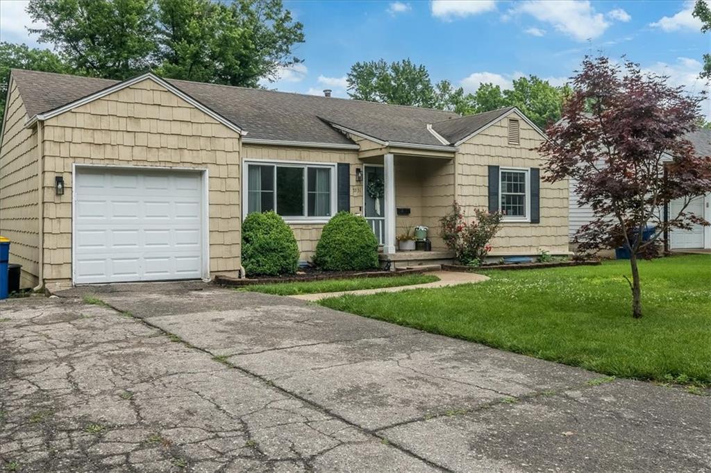 Single-story beige house with a white garage, covered entry, and cracked driveway.