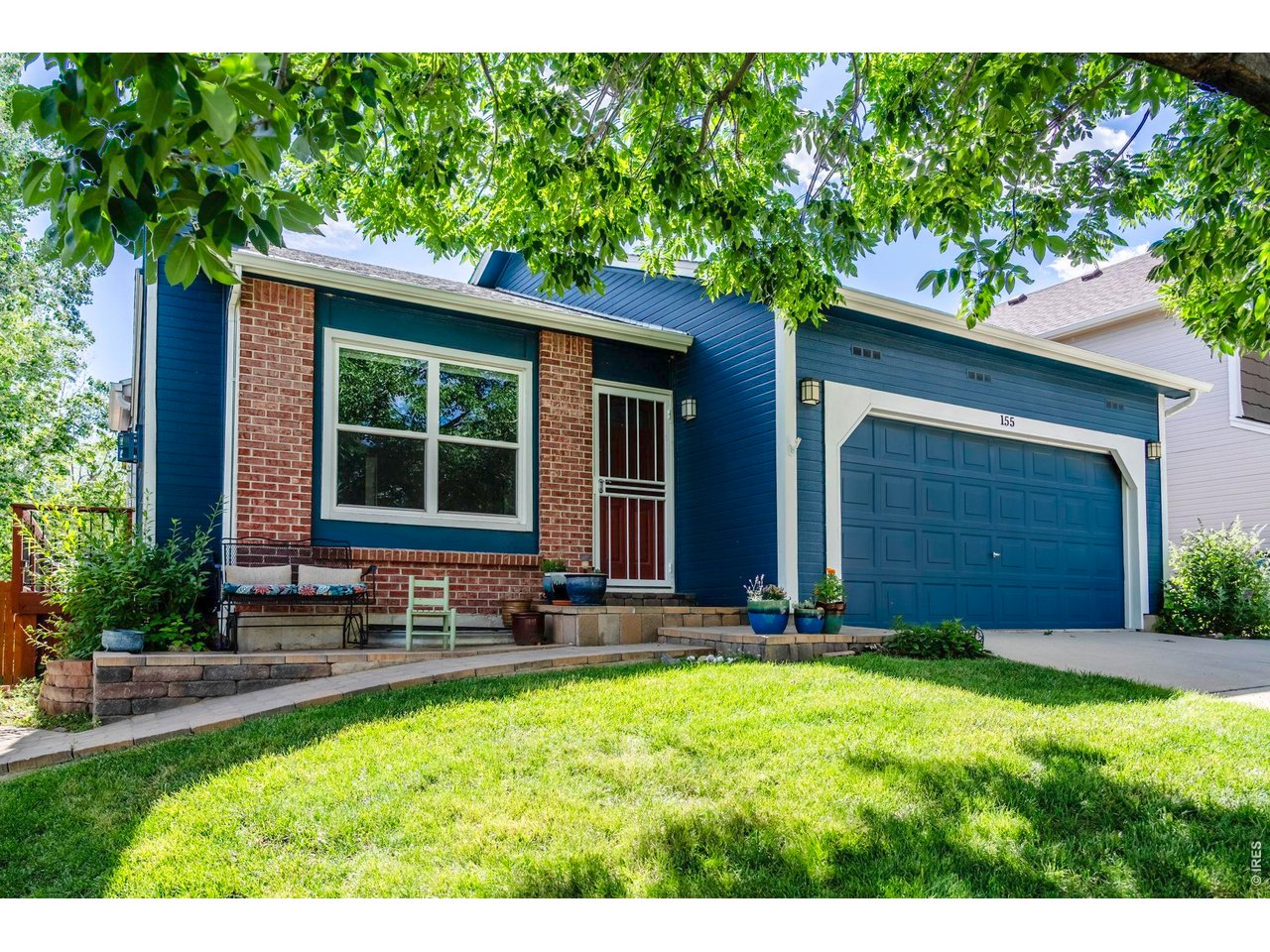 Blue house with brick accents, a two-car garage, and a shaded front lawn.