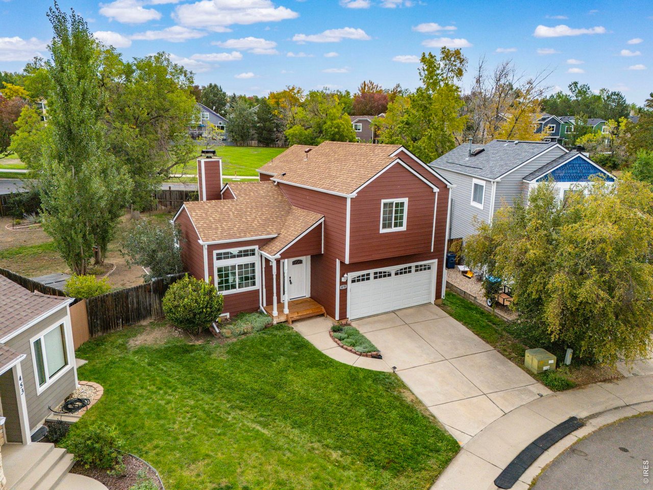 Red two-story house with white trim, attached garage, and wide driveway, seen from above.
