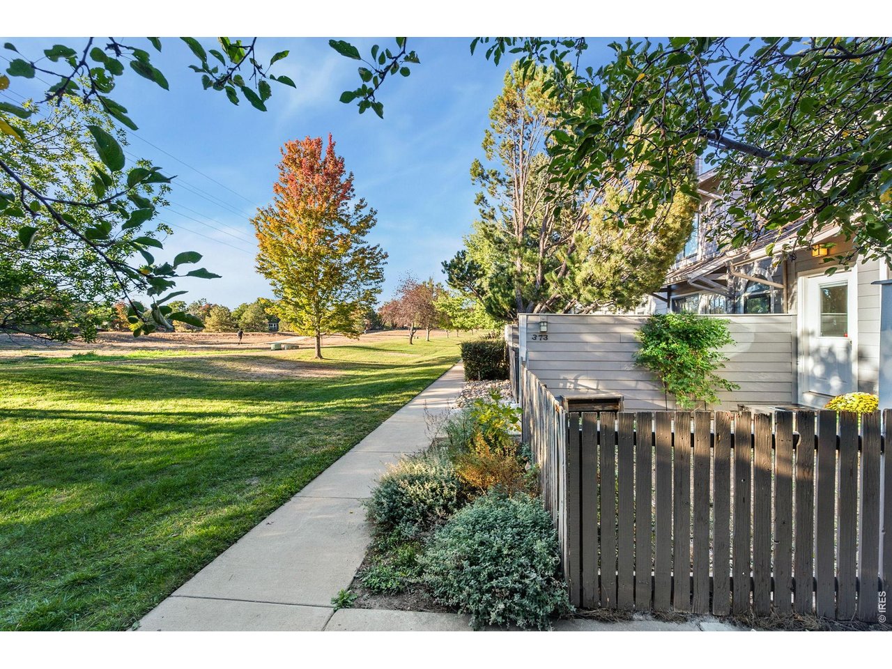 Townhouse patio beside a grassy park, with a paved path and autumn-colored trees.