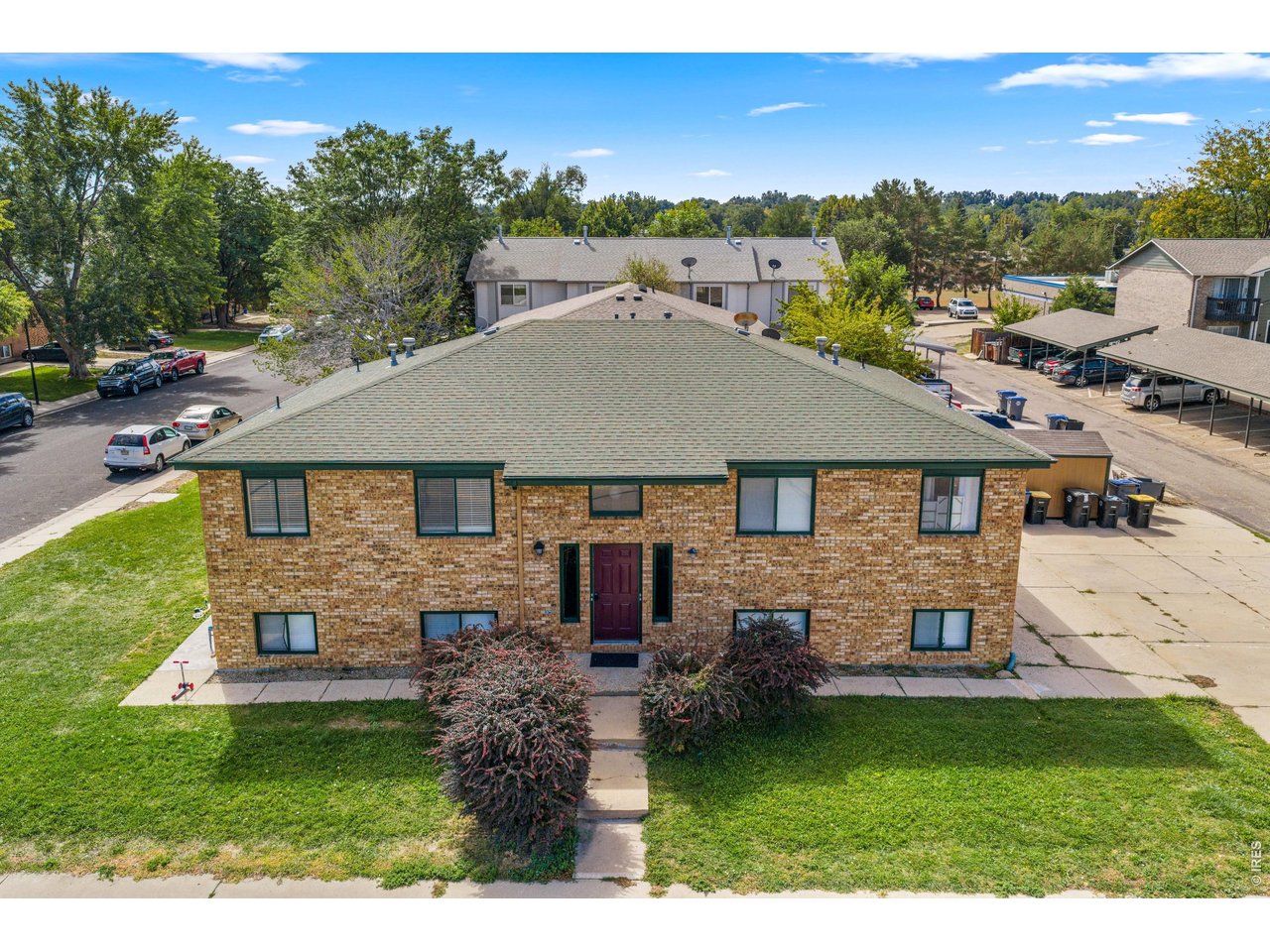 Two-story brick residential building with a broad roof, burgundy entry door, and landscaped front lawn.