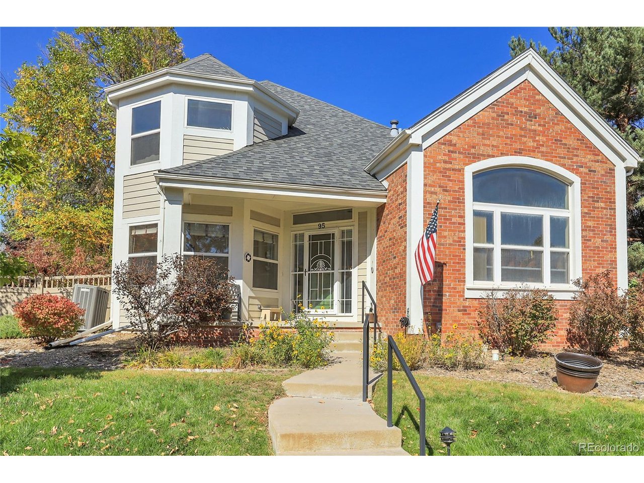 Windsor home with a red-brick gable, gray siding, American flag, and curved front walkway.