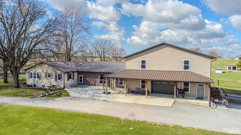 Large tan home with a stone-sided wing, metal roofs, and a covered porch on a grassy lot.