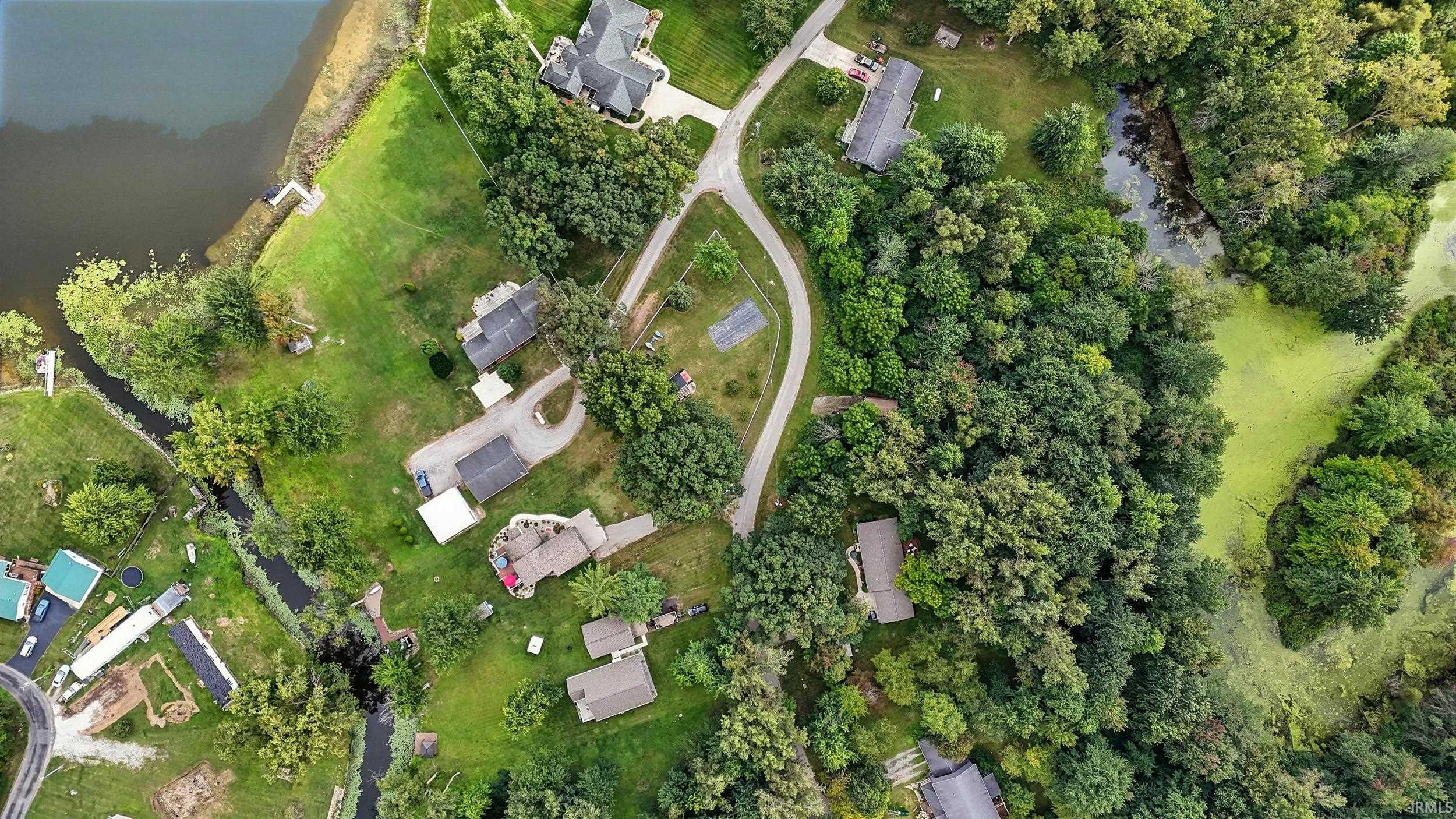 Aerial neighborhood with homes among trees, a winding road, lake, and stream.