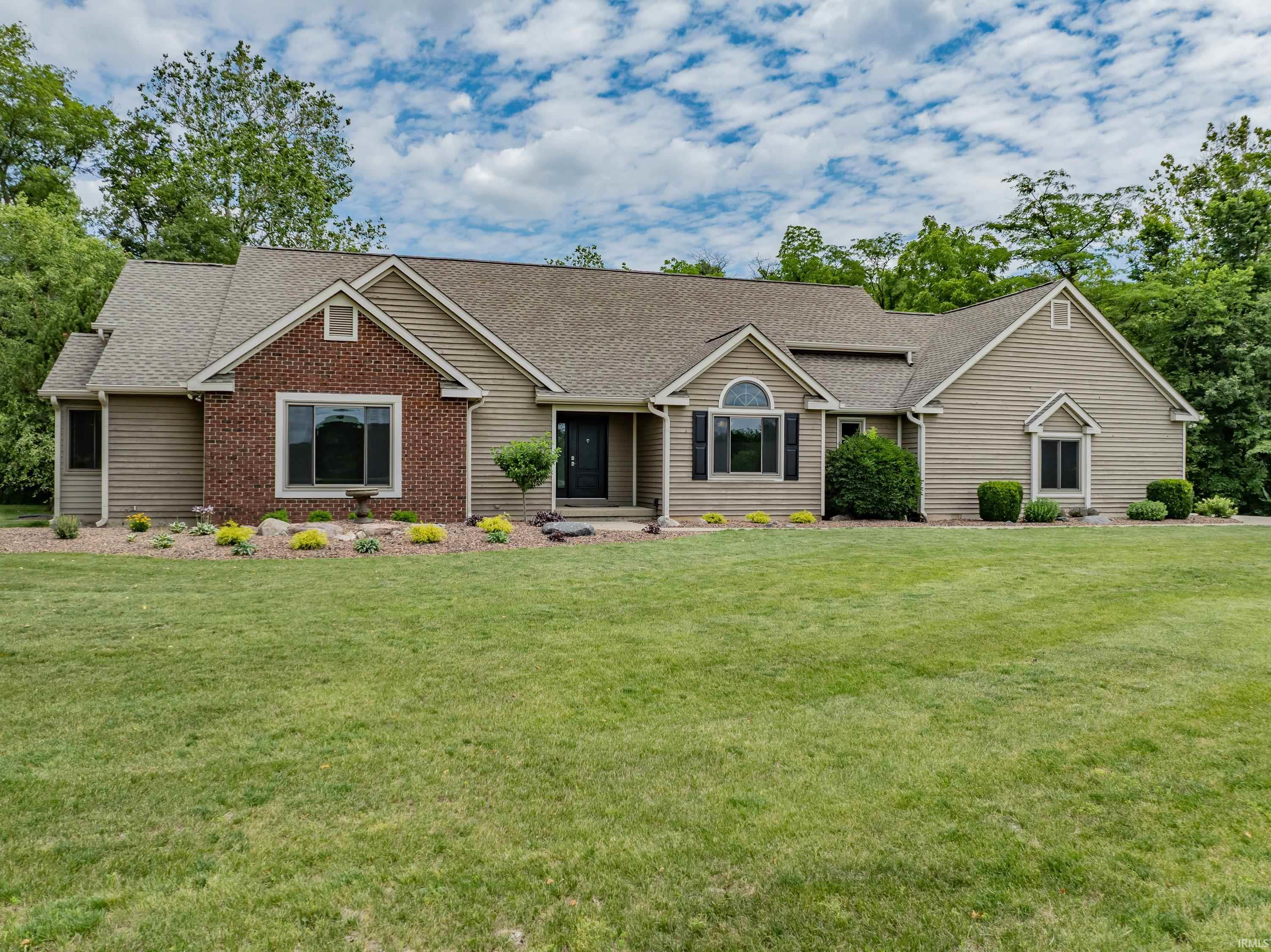 Single-story tan and brick house with a broad lawn and mature trees.
