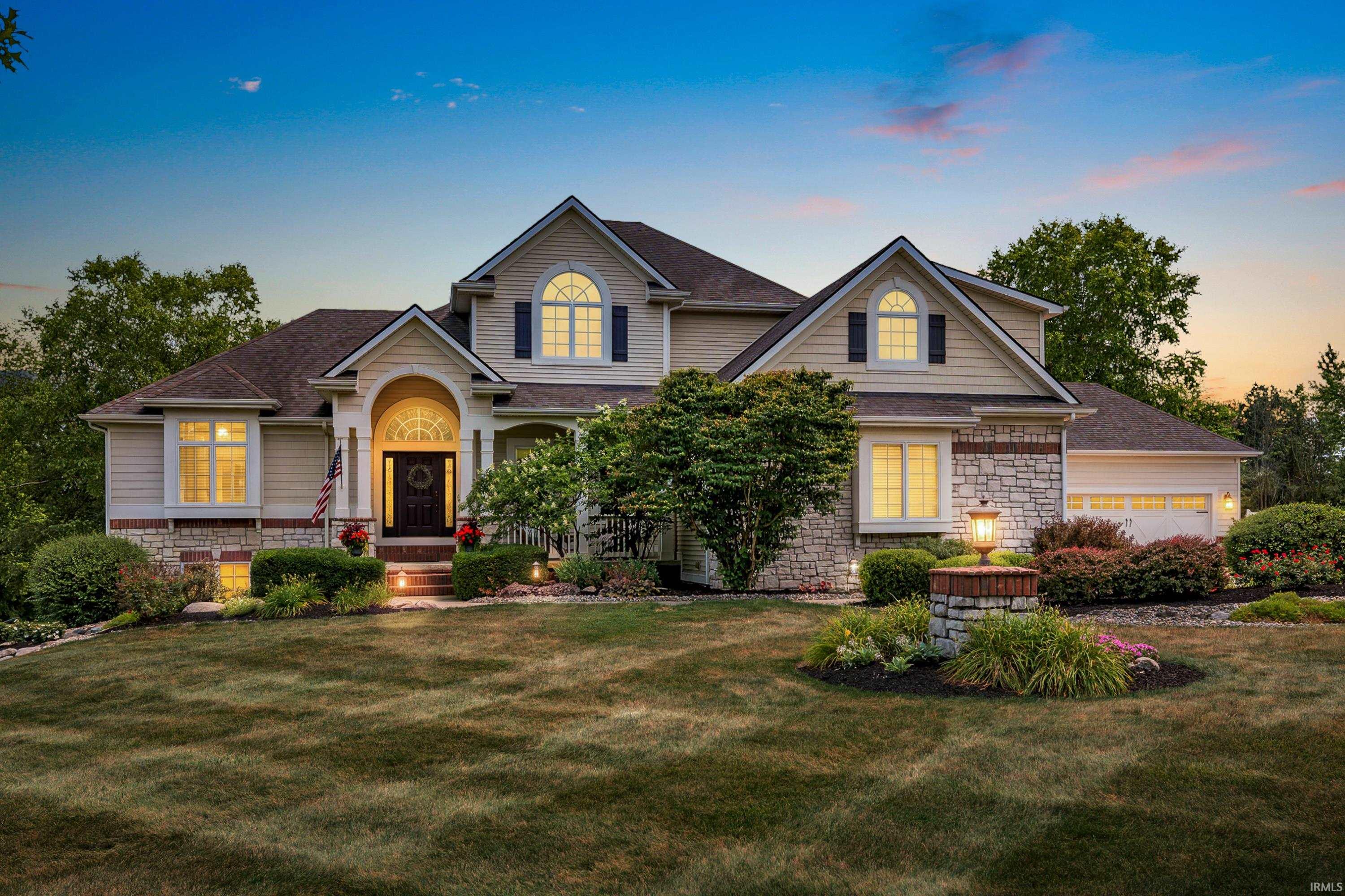 Two-story home with stone accents, arched windows, and a landscaped lawn at dusk.