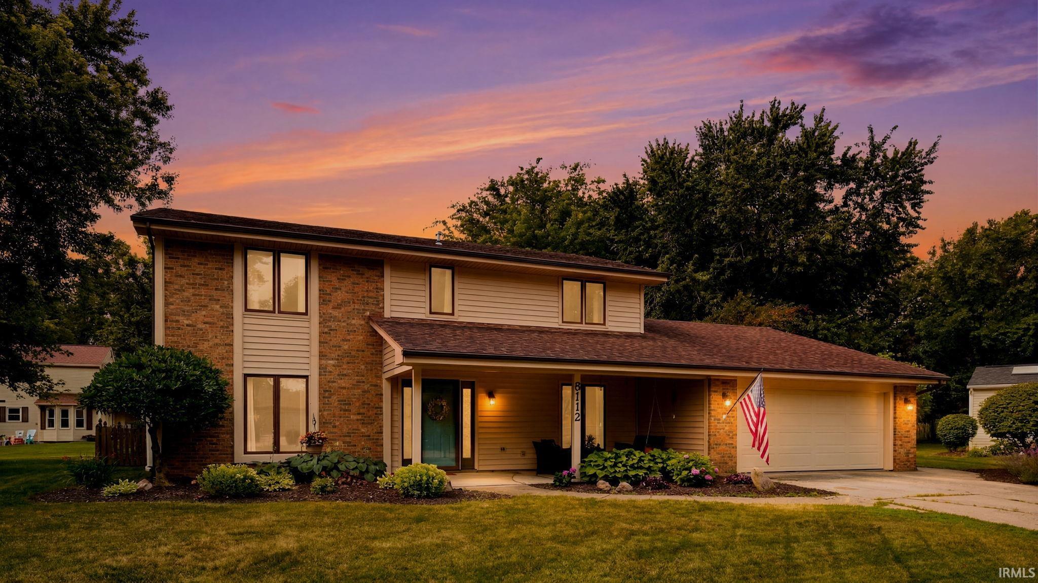 Two-story brick-and-siding home with an attached garage and American flag at sunset.