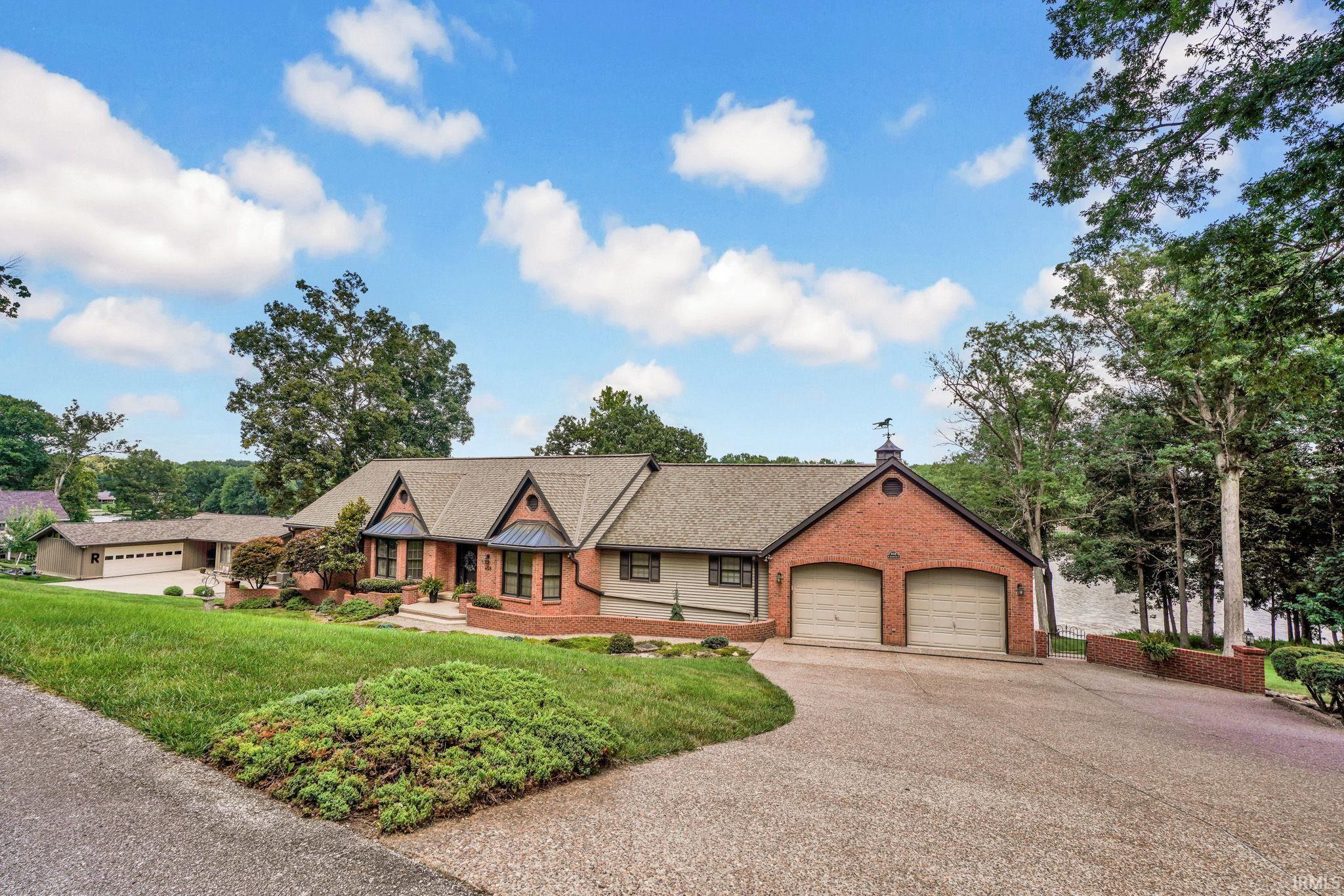 Brick-and-siding home with two garage doors, landscaped lawn, and water behind the trees.