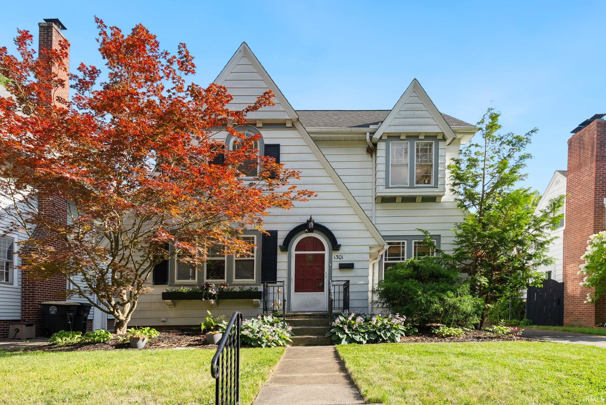 White gabled house with a red arched front door, framed by autumn foliage.