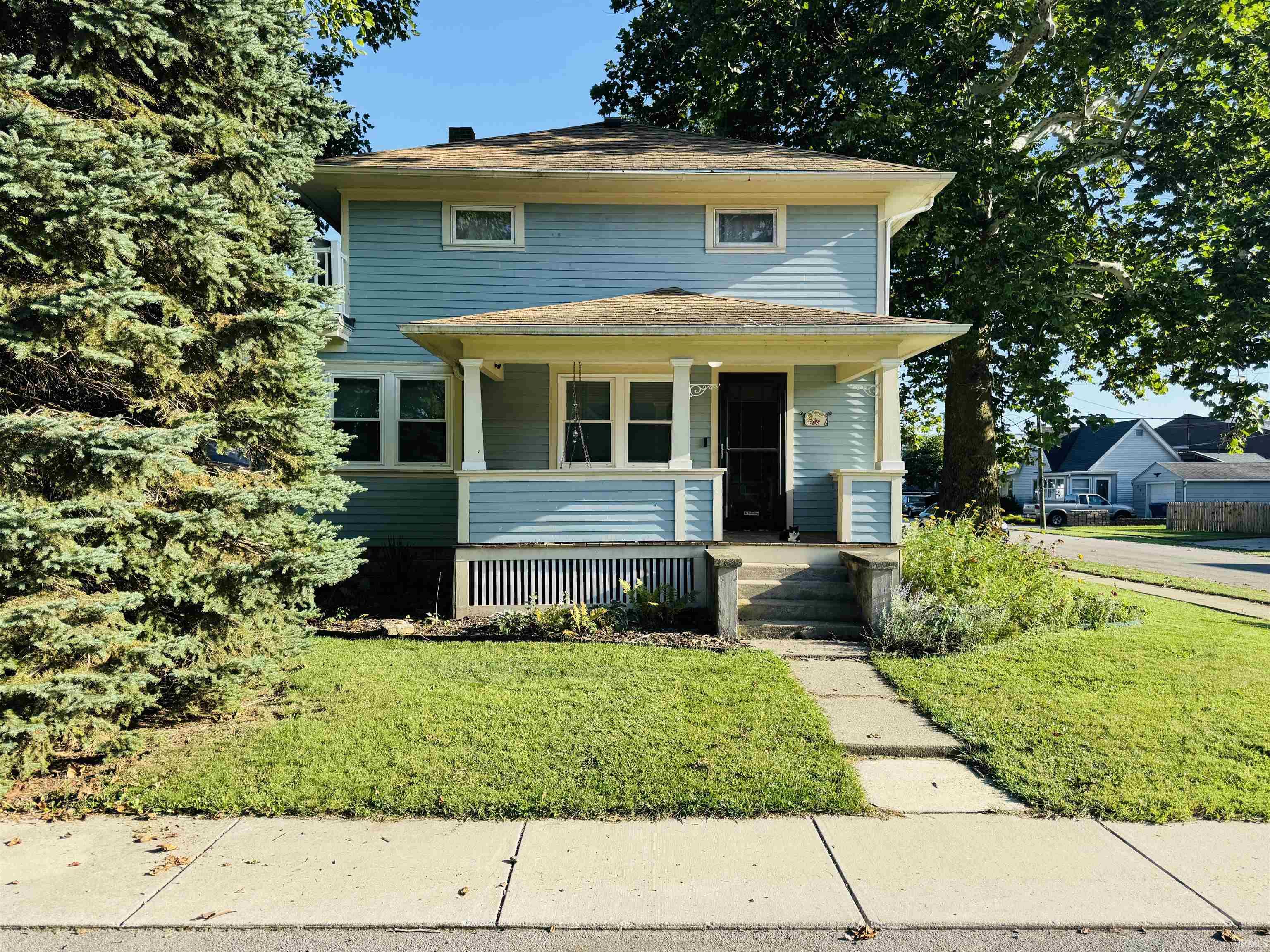 Blue two-story house with a covered porch, green lawn, and mature trees.